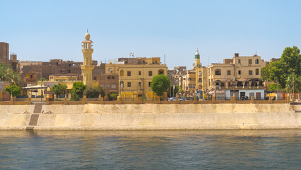 Obraz premium Traditional arab village on the west bank side of the river Nile, Egypt, with two visible minarets. Blue sky on the background.