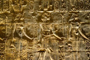 Egyptian shapes, figures and hieroglypics in relief, on a dark wall with light shadows in the...