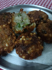 Crispy golden sabudana vadas served on a steel plate with a broken piece showing the soft inside filled with green chilies and herbs.