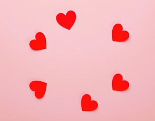 the image features a background with a soft pink hue, there are five red heart shaped cutouts scattered across the image, each of a different size and shape