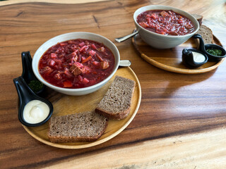 Two bowls with Traditional Russian borscht soup served in bowls with rye bread, sour cream and herbs on wooden table