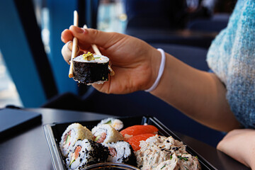 Closeup of the person hand picking up a sushi roll with chopsticks over a black tray in a modern...