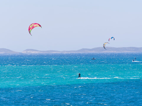 Lone kitesurfer on vivid blue ocean with distant hills and large kite visible against the sky. Paros island, Greece