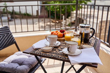 Elegant morning breakfast setting: coffee, juice, fruits, and cups on a balcony table