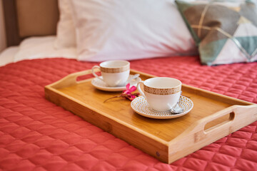 Cozy bedroom setting with tea cups on wooden tray and red quilted bedspread