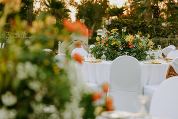 Wedding reception table decorated with orange roses, white flowers, and greenery. Elegant floral arrangement creating festive and romantic atmosphere. Ideal for wedding decoration and celebration