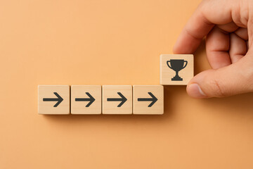 A concept achievement and steady progress is illustrated by moving an arrow block toward a trophy symbol on a soft orange background