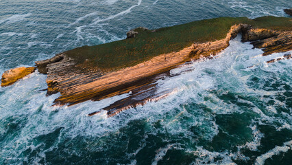 Aerial view of rugged cliffs meet the turbulent sea, the relentless waves crashing against the ancient rocks in a mesmerizing display of nature's power, Baleal, Leiria District, Portugal.