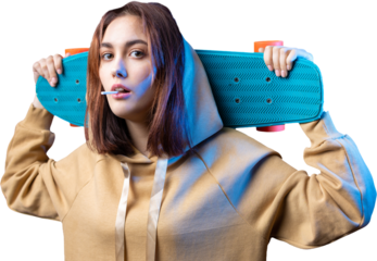 Young beautiful fashionable hipster girl dressed in a hoodie holds a skateboard in her hands on a purple studio background. Eats a lollipop.