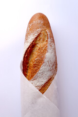 Well-baked brown baguette bread wrapped in white paper.