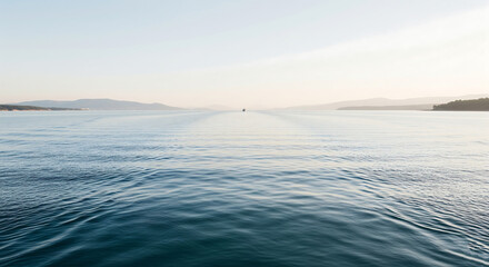 A serene view of the ocean with a distant boat leaving a wake under a clear sky