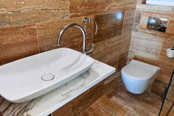Modern bathroom design with vessel sink and wall-mounted toilet in natural stone decor