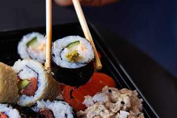 Chopsticks grasping sushi roll with cucumber, avocade and salmon. Maki  being picked up with...