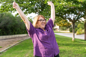 Senior woman joyfully raising arms, radiating happiness while embracing wellness during outdoor park moment