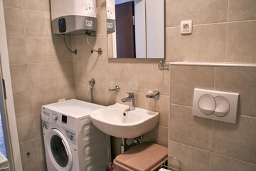 Modern compact bathroom with washer sink heater mirror and beige tiles