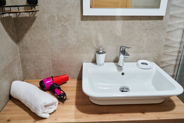 Modern bathroom sink with vanity items towel and hair dryer on wooden counter