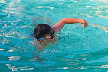 Child with glasses swimming in a pool.