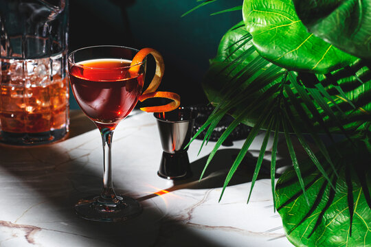 Richly colored cocktail garnished with orange peel sits on marble countertop in a stylish setting after sunset