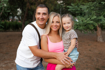 Smiling mother and dad holding cute child daughter outdoors close up. Looking at camera. Parenthood.