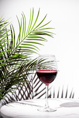 Elegant glass of red wine with green palm leaves in a bright, modern setting creating a luxurious...