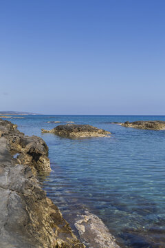 View of the rocky coast meeting the turquoise sea under a clear blue sky, with sun-kissed textures and distant shores, Dipkarpaz, Northern Cyprus, Cipro.