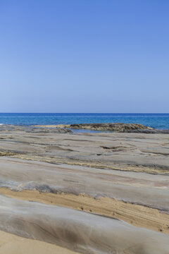 View of the rocky beach meets the tranquil turquoise sea under a clear blue sky, creating a serene coastal scene, Dipkarpaz, Northern Cyprus, Cipro.