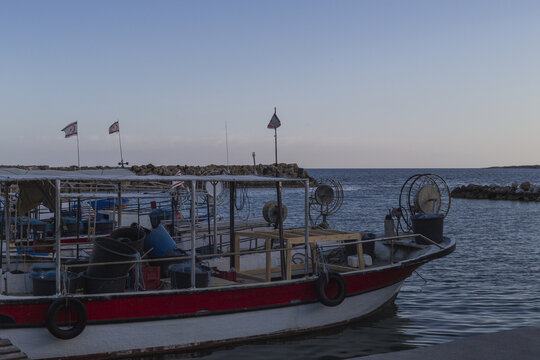 View of a red and white fishing boat sits peacefully in the harbor, reflecting the soft light of dusk on the calm waters, Dipkarpaz, Northern Cyprus, Cipro.