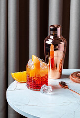Negroni sbagliato cocktail served on a marble table with orange slices and a cocktail shaker in...