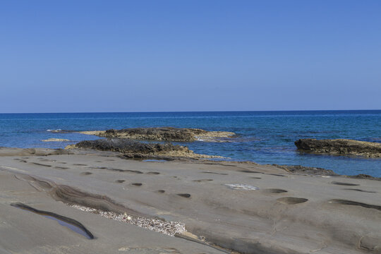 View of the rugged, sun-baked shoreline meets the turquoise sea under a clear blue sky, a tranquil coastal scene, Dipkarpaz, Northern Cyprus, Cipro.
