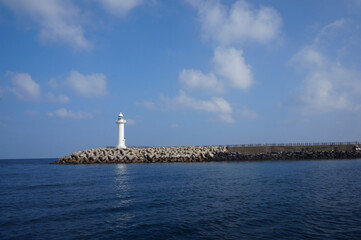 White lighthouse at the end of breakwater under a bright blue sky