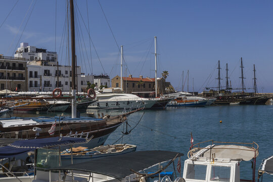 Girne, Cyprus - 25 June 2025: View of the harbor's tranquil waters reflecting the azure sky, cradling elegant yachts and historic ships against the backdrop of white buildings.