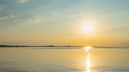 Obraz premium golden sunset on lake Constance, with small waves and illuminated little clouds, sun star reflected in water surface, orange and yellow dominant over blue, waiting for sunset