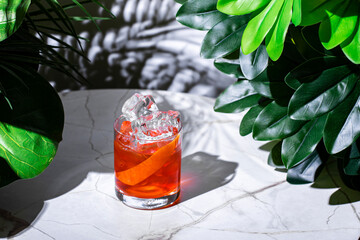 Vibrant negroni cocktail surrounded by lush greenery on a marble surface in a cozy afternoon setting