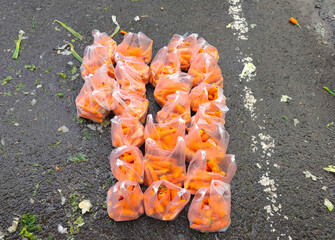 Plastic bags filled with fresh carrot are neatly arranged on a wet asphalt surface at a traditional market. A vivid snapshot that reflects local produce trade and everyday street market