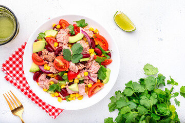 Mexican style salad with canned tuna, avocado, corn, red beans, cherry tomatoes and cilantro, white table background, top view
