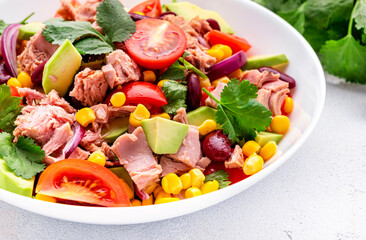 Mexican style salad with canned tuna, avocado, corn, red beans, cherry tomatoes and cilantro, white table background, top view