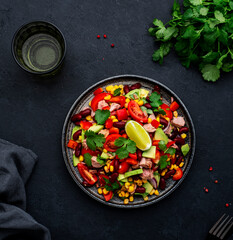 Tex-mex salad with canned tuna, avocado, corn, red beans, cherry tomatoes, cilantro and lime dressing, black table background, top view