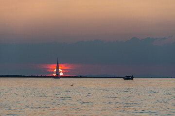 Sunset with sailing ship, boat on Lake Constance, red and orange sunset above the waves on the lake, the sun sets in a cloud over the water surface, beautiful sunset