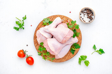 Raw chicken legs or drumsticks on wooden board with pepper, salt and parsley, top view