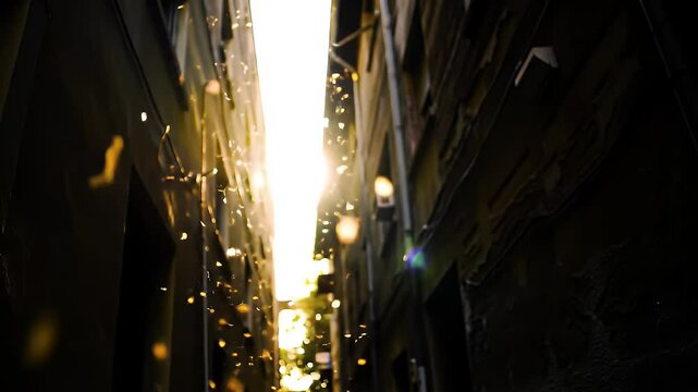 Slow-motion video of golden sunlight piercing through an alleyway between old buildings, illuminating floating dust particles in the air.

