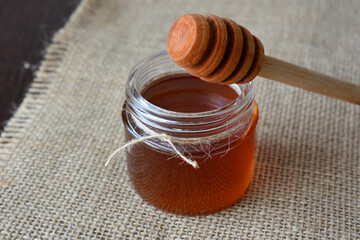 Jar of Honey with Wooden Dipper on Burlap Surface close up