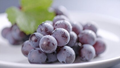 Juicy bunny of ripe blue grapes on a white plate, decorated with fresh green leaves. Drops of water are visible on the berries, emphasizing their freshness and natural beauty.