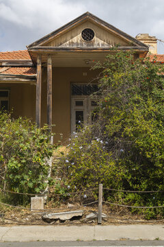 View of an old, weathered building facade overtaken by lush green foliage under a cloudy sky, a forgotten corner of Varosha, Famagusta, Cyprus.