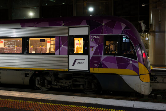 Side view of the exterior of a Vline Vlocity train's rear carriage, with its interior illuminated, sitting at Southern Cross Station at night