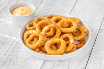 Crispy onion rings with cheese sauce on white plate and table