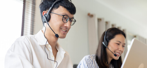 close up asian man call center agent wear headset device and smiling working in operation room with service-mind at desktop table , telemarketing and help desk concept