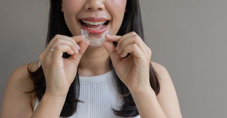 close up young asian beautiful woman smiling with hand holding dental aligner retainer (invisible) at dental clinic for beautiful teeth treatment course concept