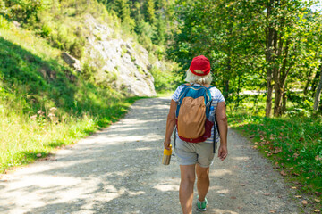 An active senior woman is seen walking alone along a scenic forest path surrounded by lush greenery...