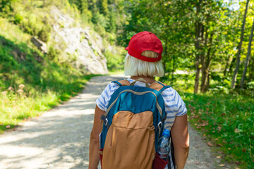 An active senior woman is seen walking alone along a scenic forest path surrounded by lush greenery...