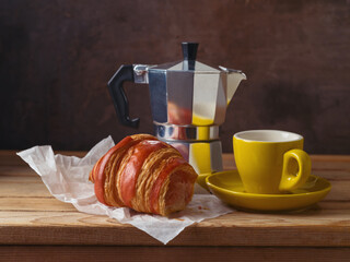 Still life with coffee cup, coffee pot and croissant on wooden table